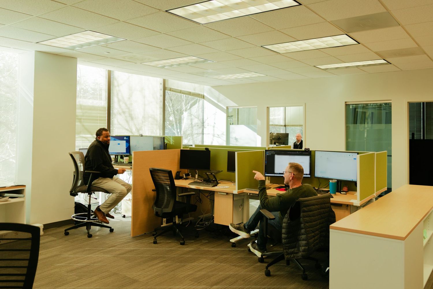 Empty modern office space with white walls, fluorescent lighting and workstations.