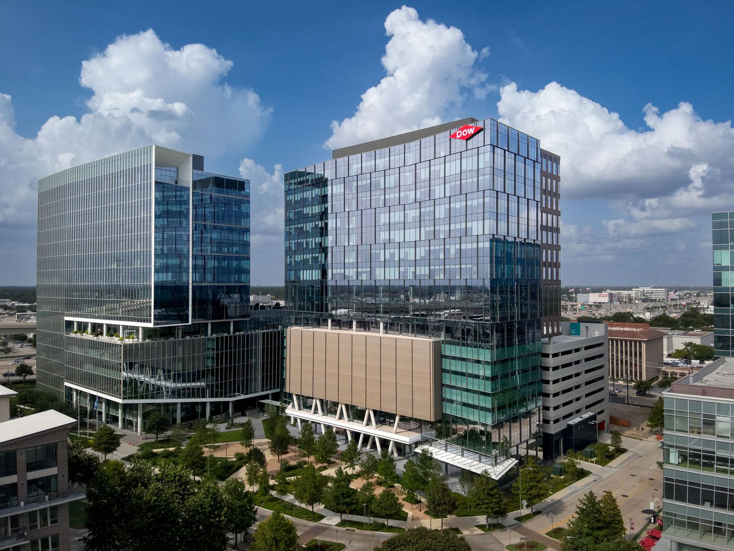 Aerial view of modern glass office buildings with a red logo sign under blue skies in an urban business district.