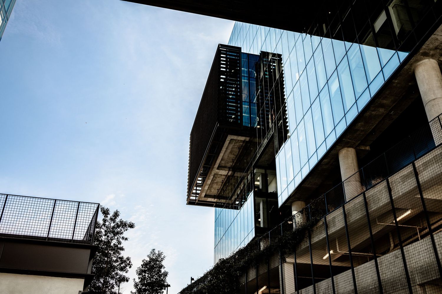 Modern glass office buildings with reflective surfaces tower against a blue sky in an urban business district.
