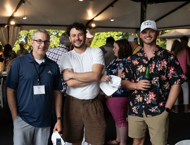Three people pose together under a covered outdoor venue during what appears to be a social gathering or event.