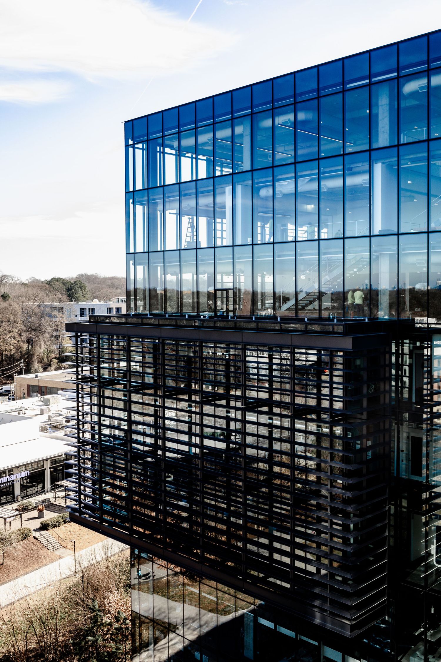 Modern glass office building with black horizontal sunshades photographed from multiple angles against a bright sky.