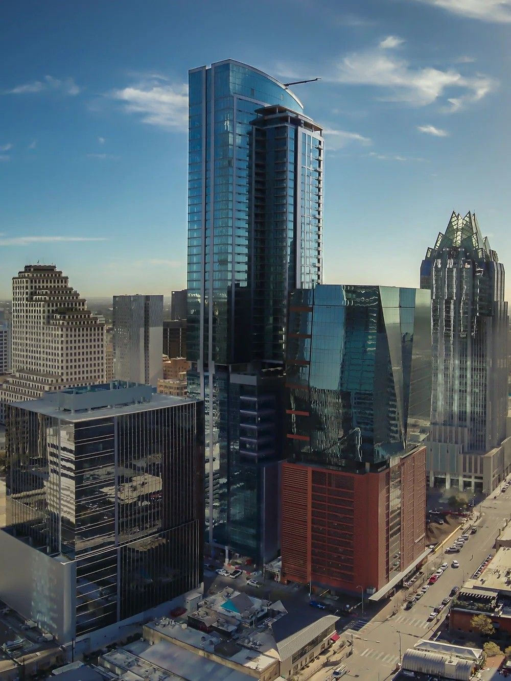 Aerial view of modern glass skyscraper under construction in downtown Austin, Texas cityscape against blue sky.