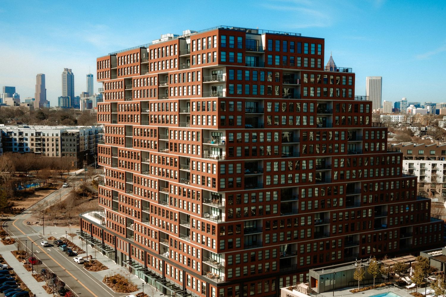 Modern brick high-rise apartment building with stepped terraces against a city skyline backdrop on a clear day.