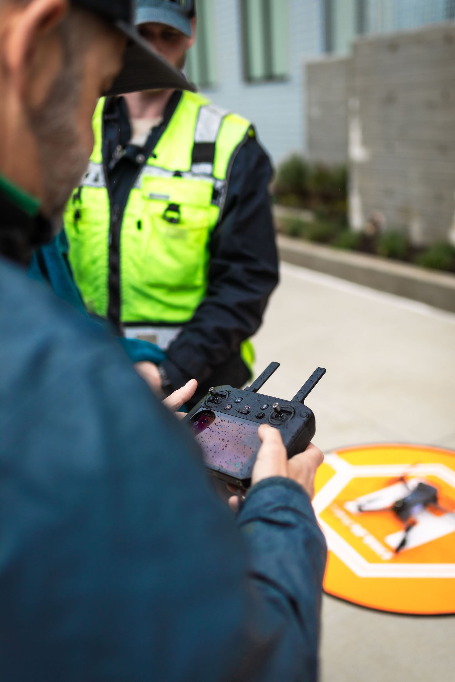 Worker operating drone controller with safety vest visible in background.