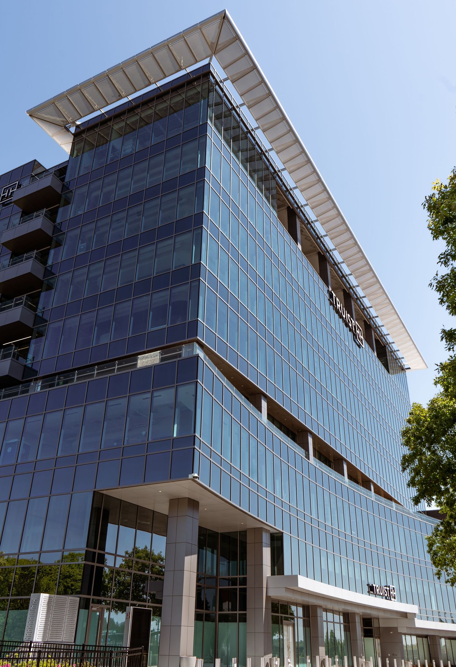 Modern glass office building with angular roof and blue-tinted windows reflecting sunlight against a clear sky.