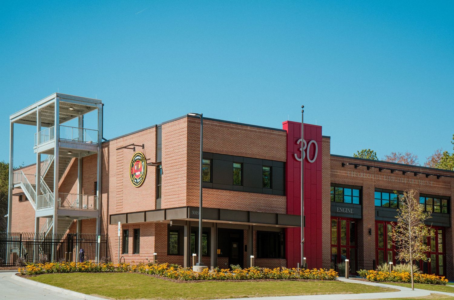 Modern brick school building with glass entrance and landscaped grounds under bright blue sky.