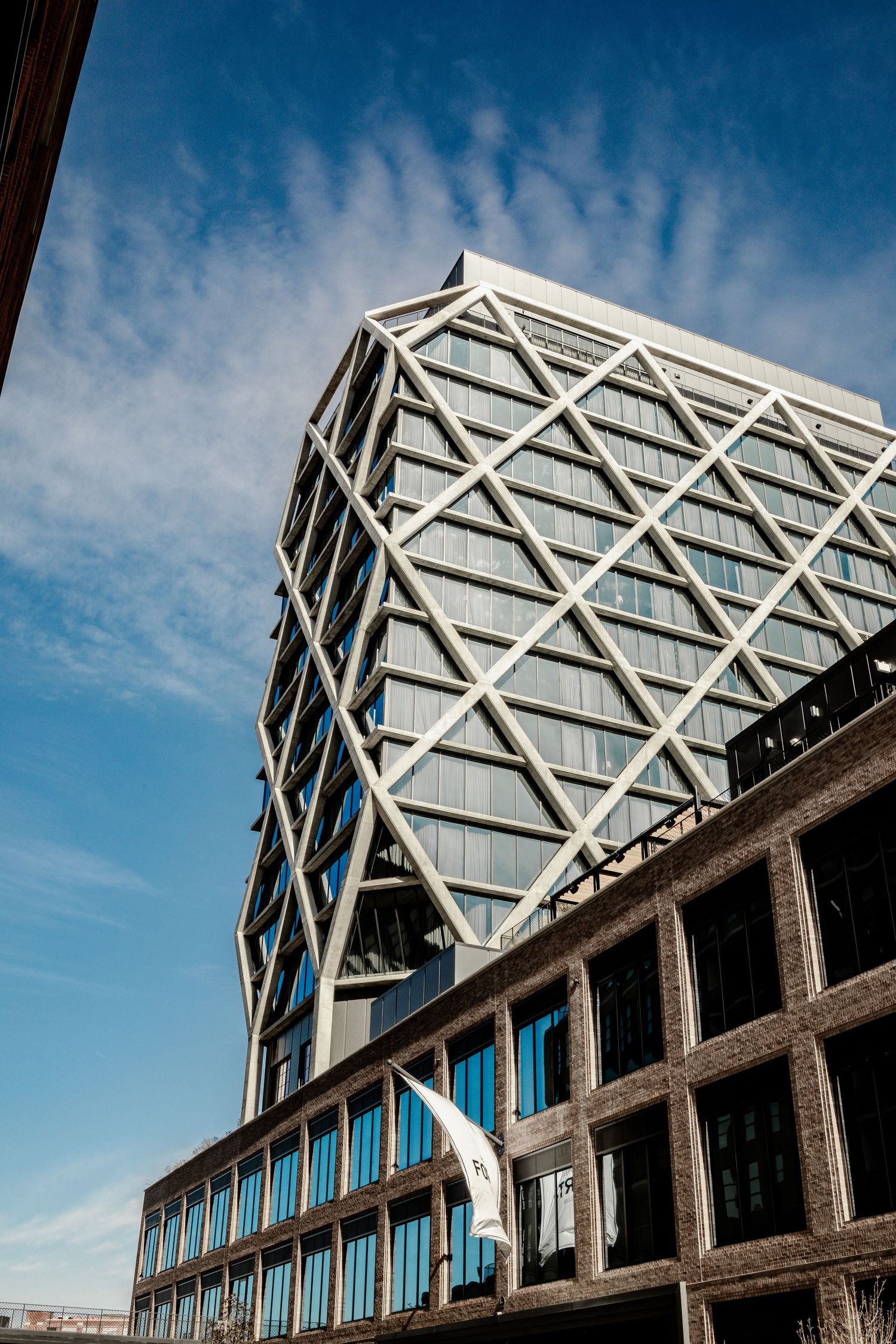 Modern office building with geometric diamond-patterned facade against blue sky with white clouds.