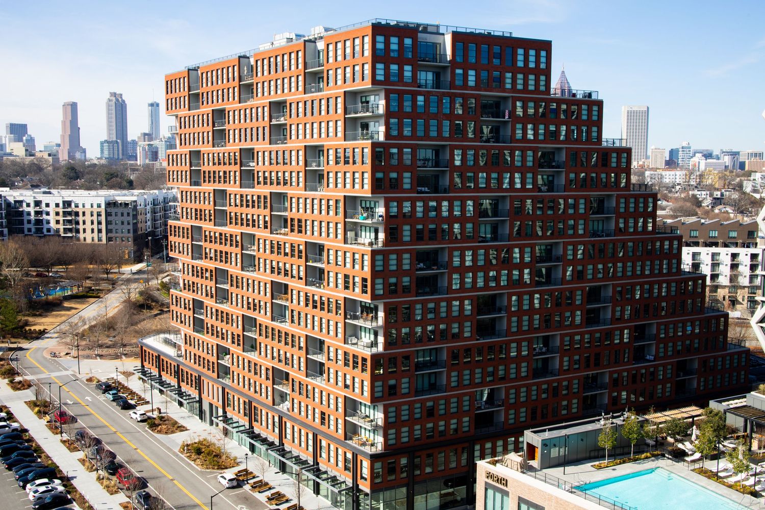 Modern stepped apartment building with red brick facade and geometric design in an urban setting with skyline views.