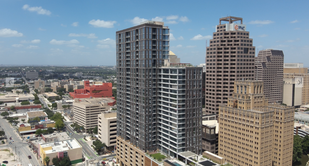 Aerial view of modern high-rise buildings in a bustling urban cityscape under a partly cloudy blue sky.