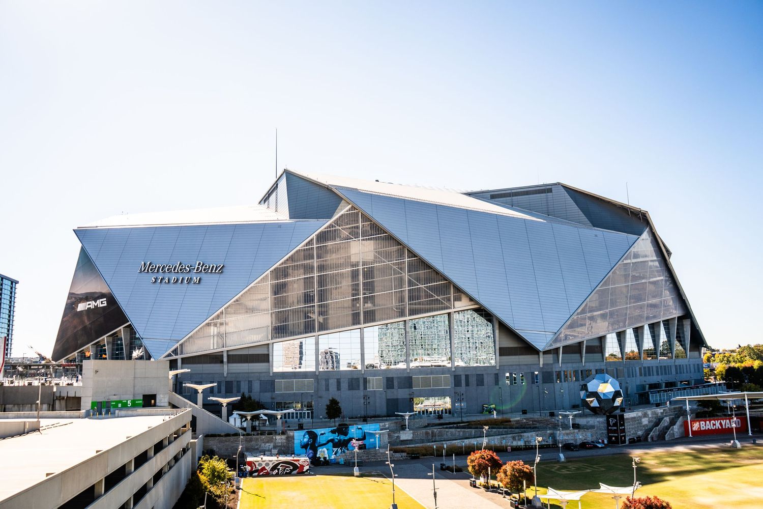 Modern warehouse buildings with angular metal roofs stand against a bright blue sky on a sunny day.