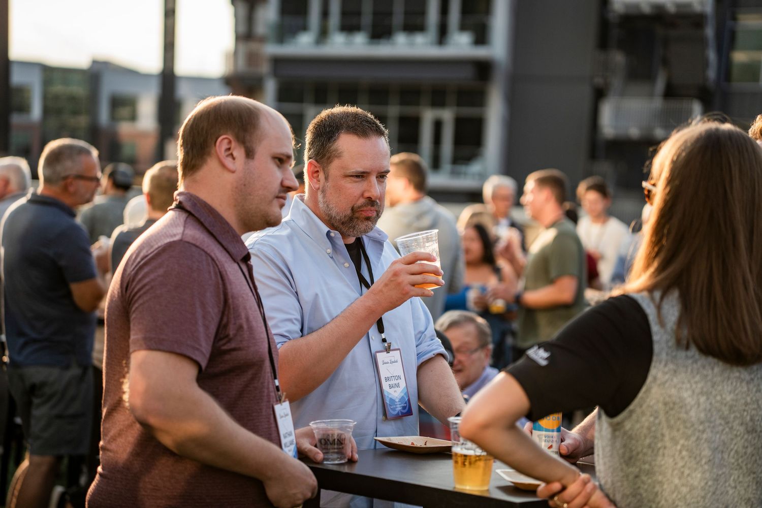A crowded outdoor social gathering with people mingling and holding drinks at a networking event.