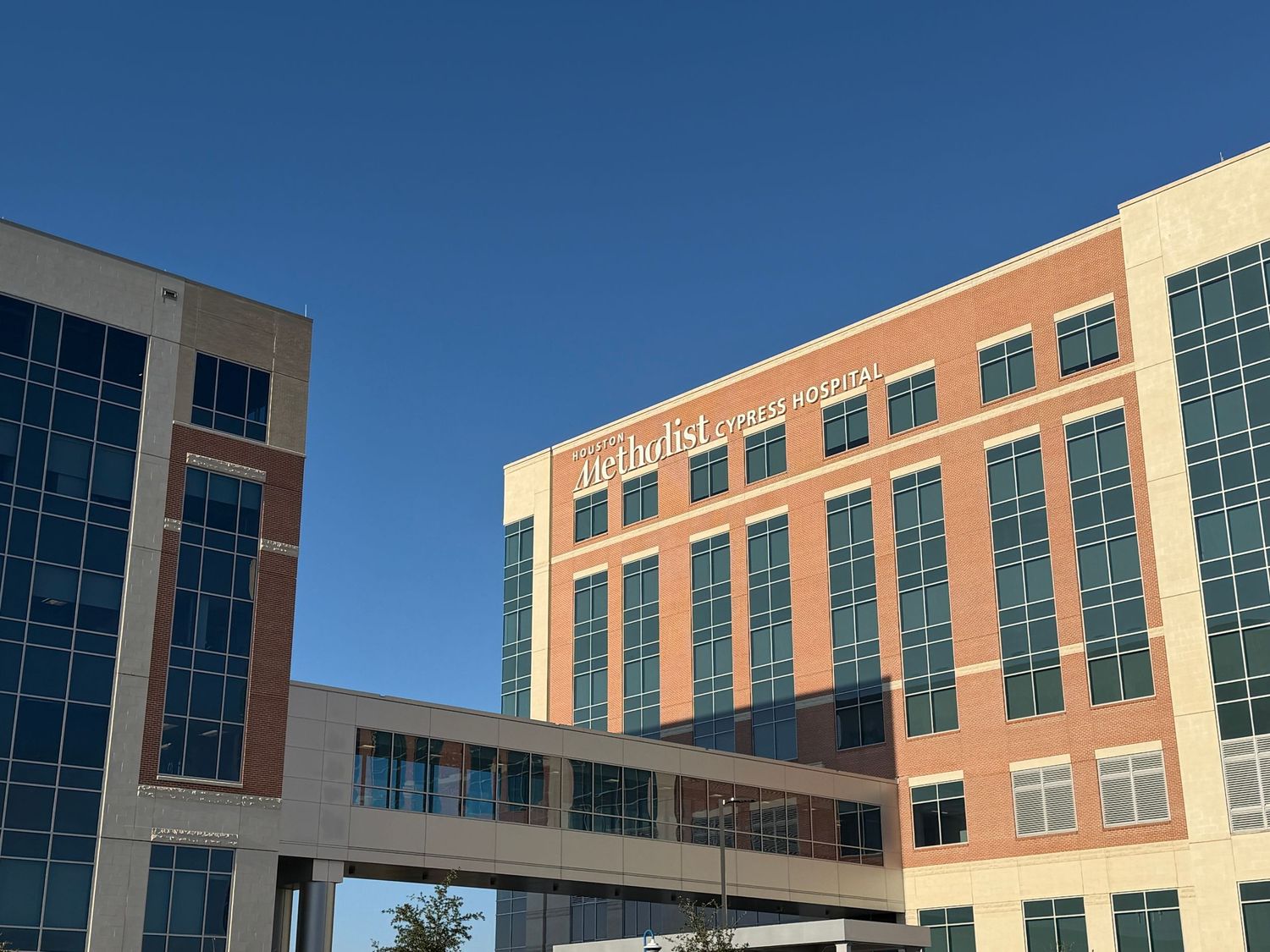 Exterior view of Methodist Frisco Hospital, a modern multi-story brick and glass building under a clear blue sky.