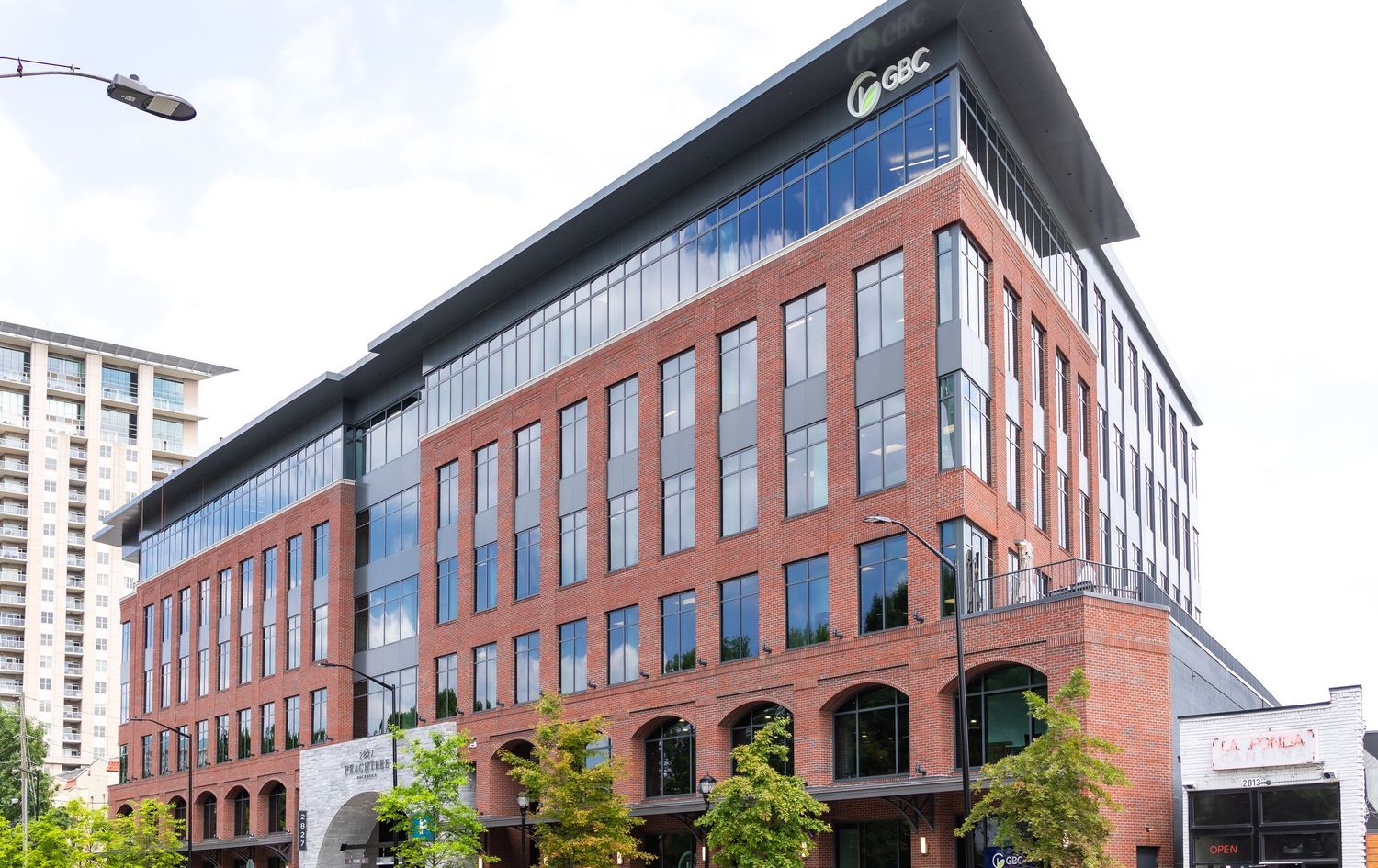 Panoramic view of modern brick commercial buildings with glass windows and landscaping along an urban street.