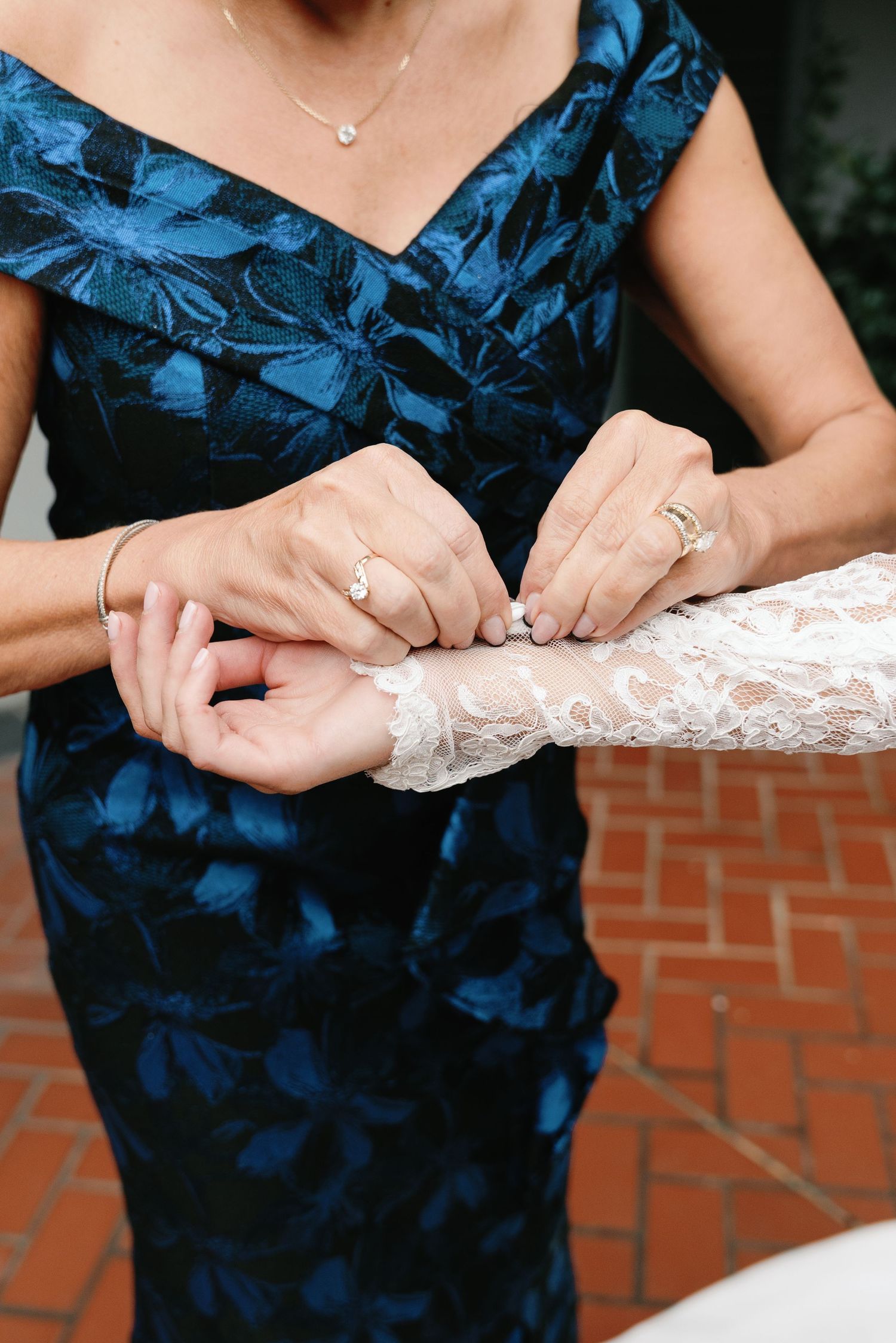 Hands adjusting a delicate lace sleeve detail against a navy blue floral dress.