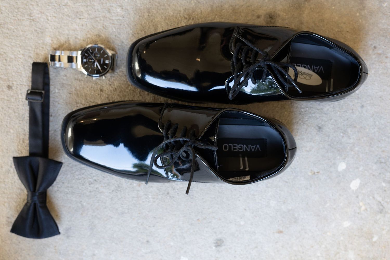 A row of shiny black patent leather dress shoes displayed on a light colored surface.