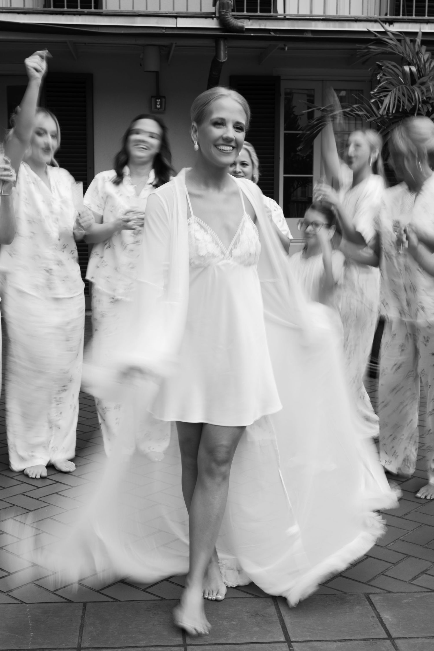 Motion-blurred black and white photograph of people in white dresses dancing at a celebration.