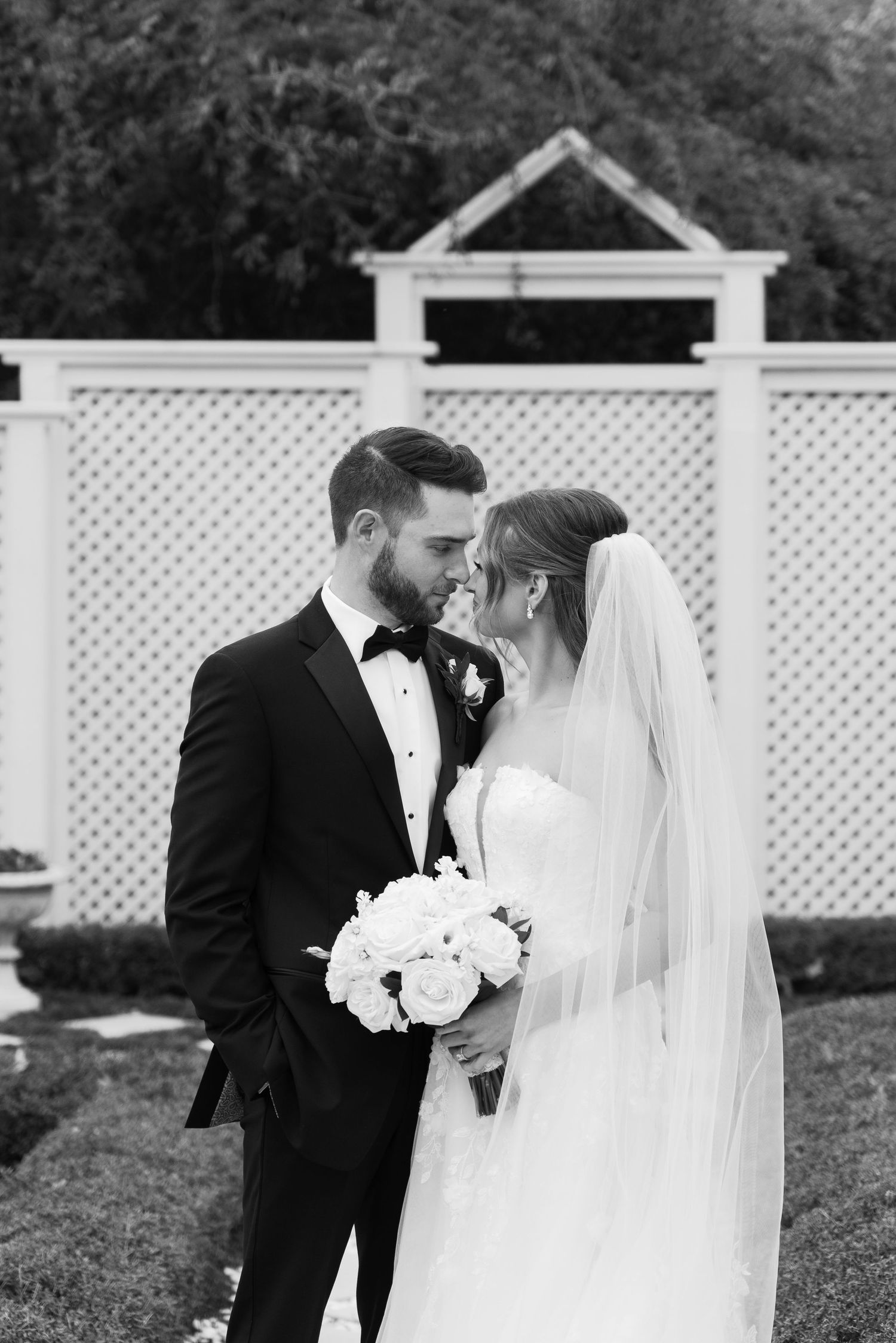 Romantic wedding portraits with bride and groom against white lattice garden backdrop.