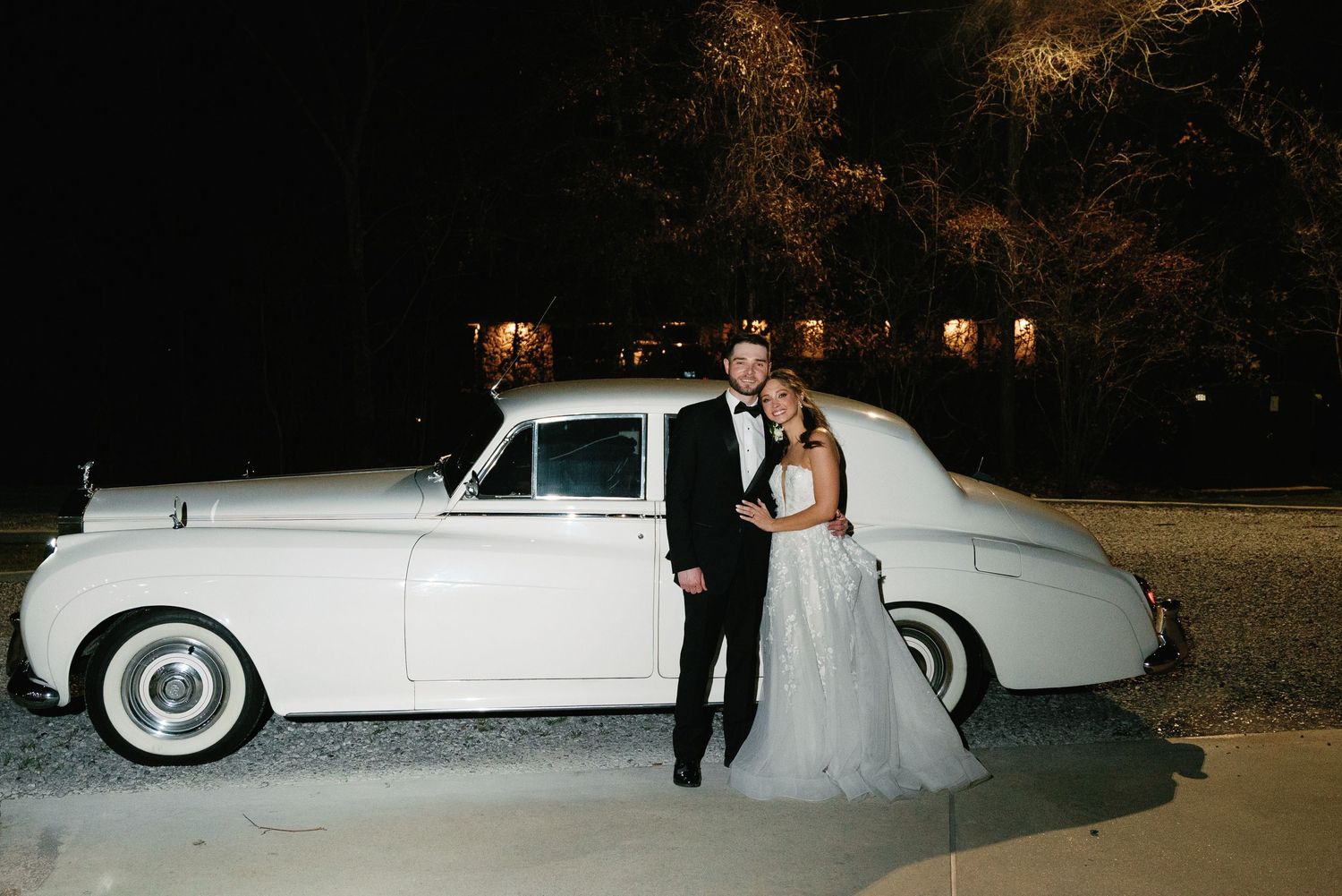 Classic white vintage car parked outside during nighttime wedding celebration.