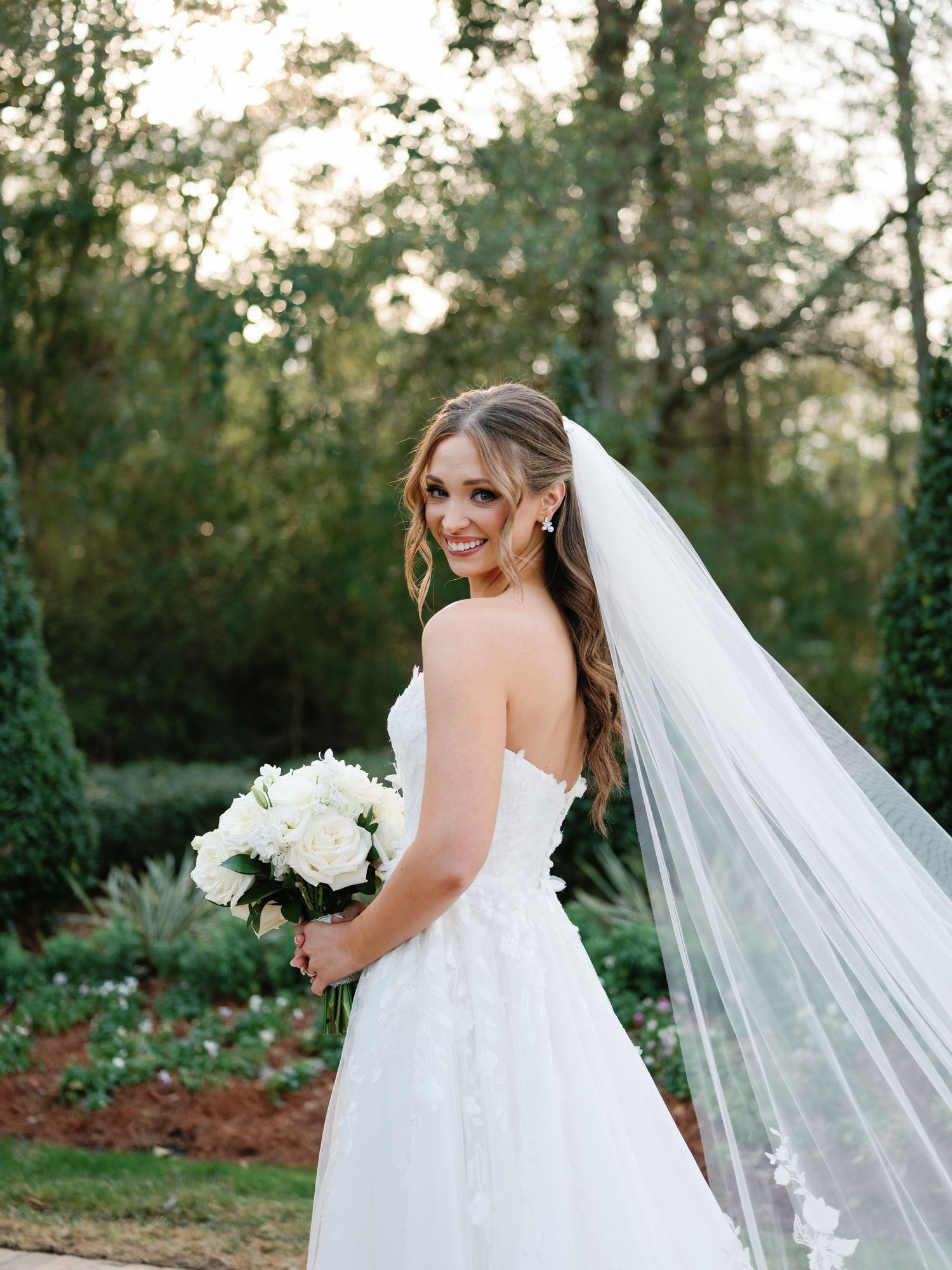 Beautiful wedding portrait in garden setting with white bouquet and flowing veil.