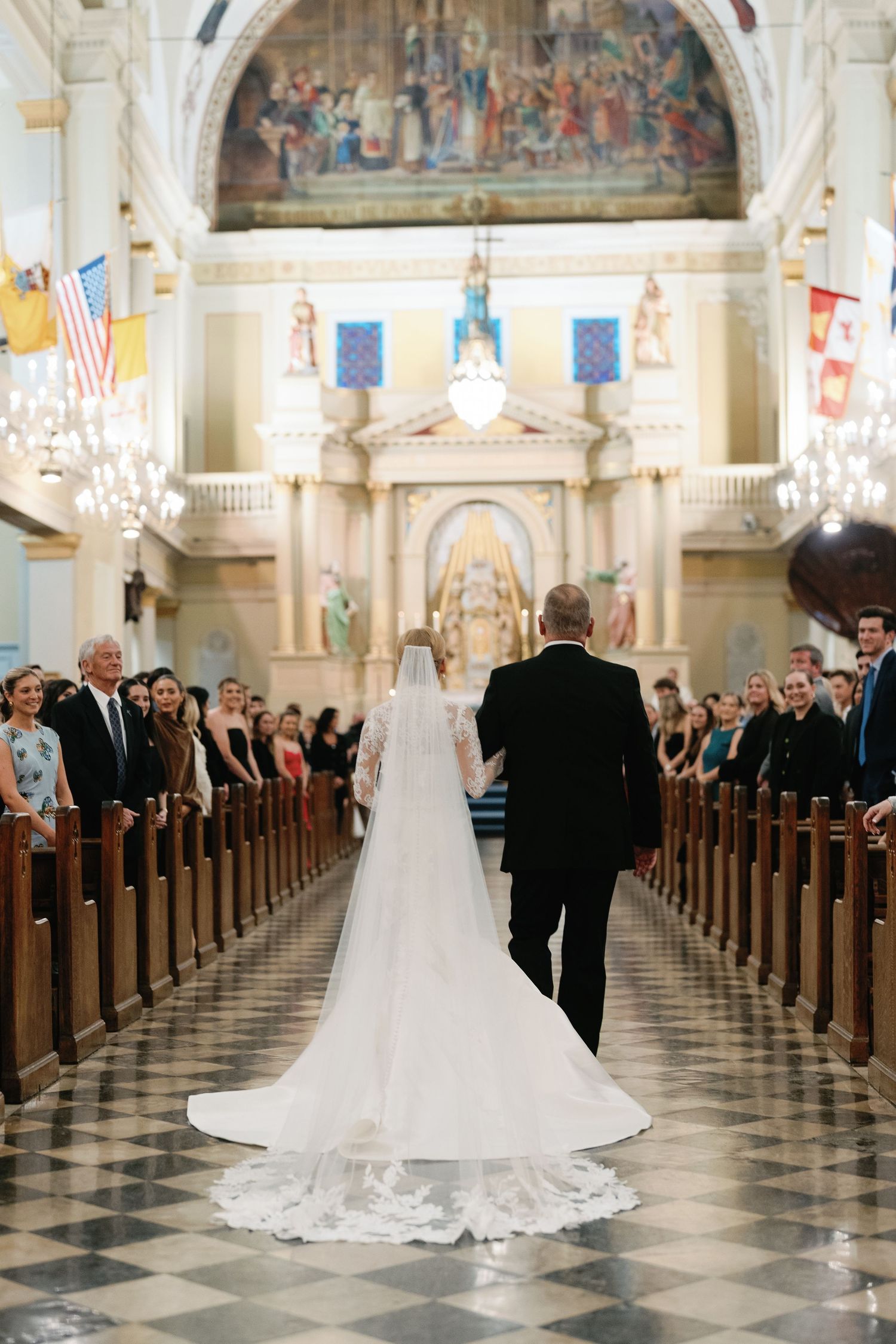 Wedding ceremony in grand cathedral with checkered floor and ornate religious artwork.