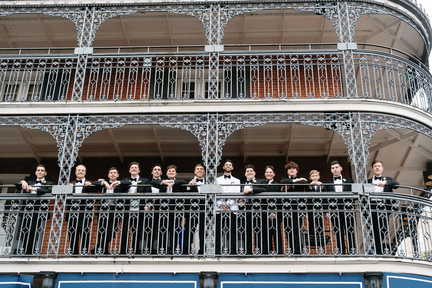 Wedding party poses on ornate iron balcony in French Quarter style architecture.