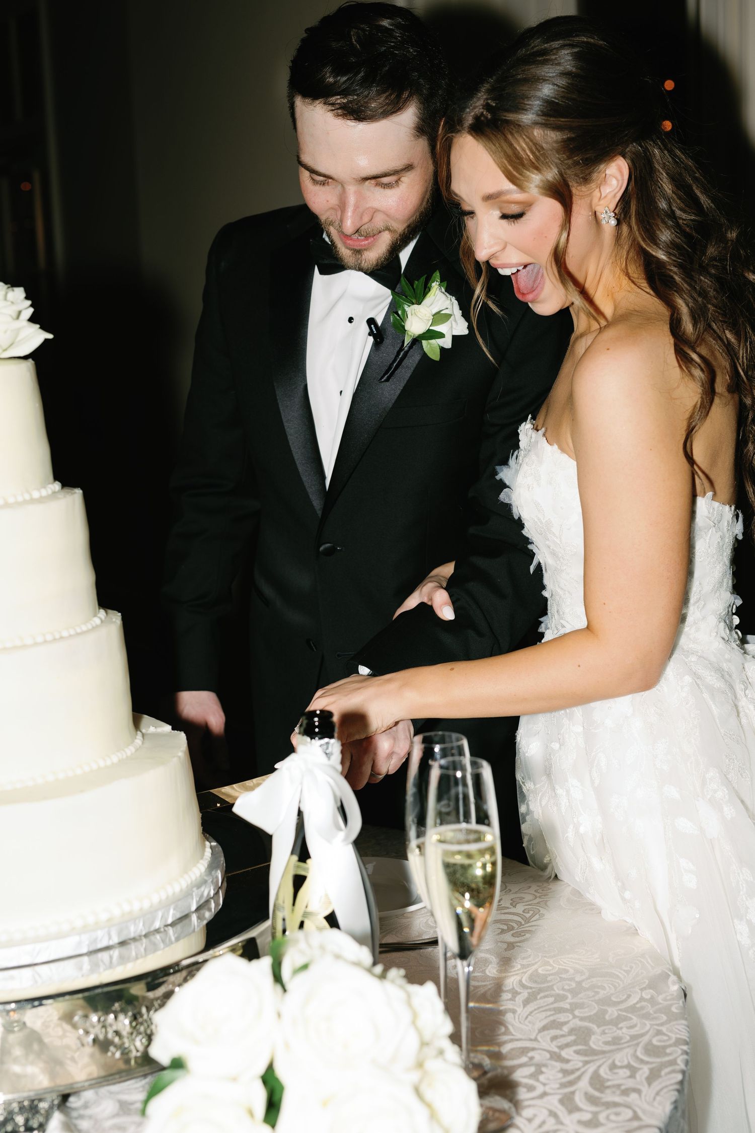 Newlyweds laugh together while cutting their elegant white wedding cake.