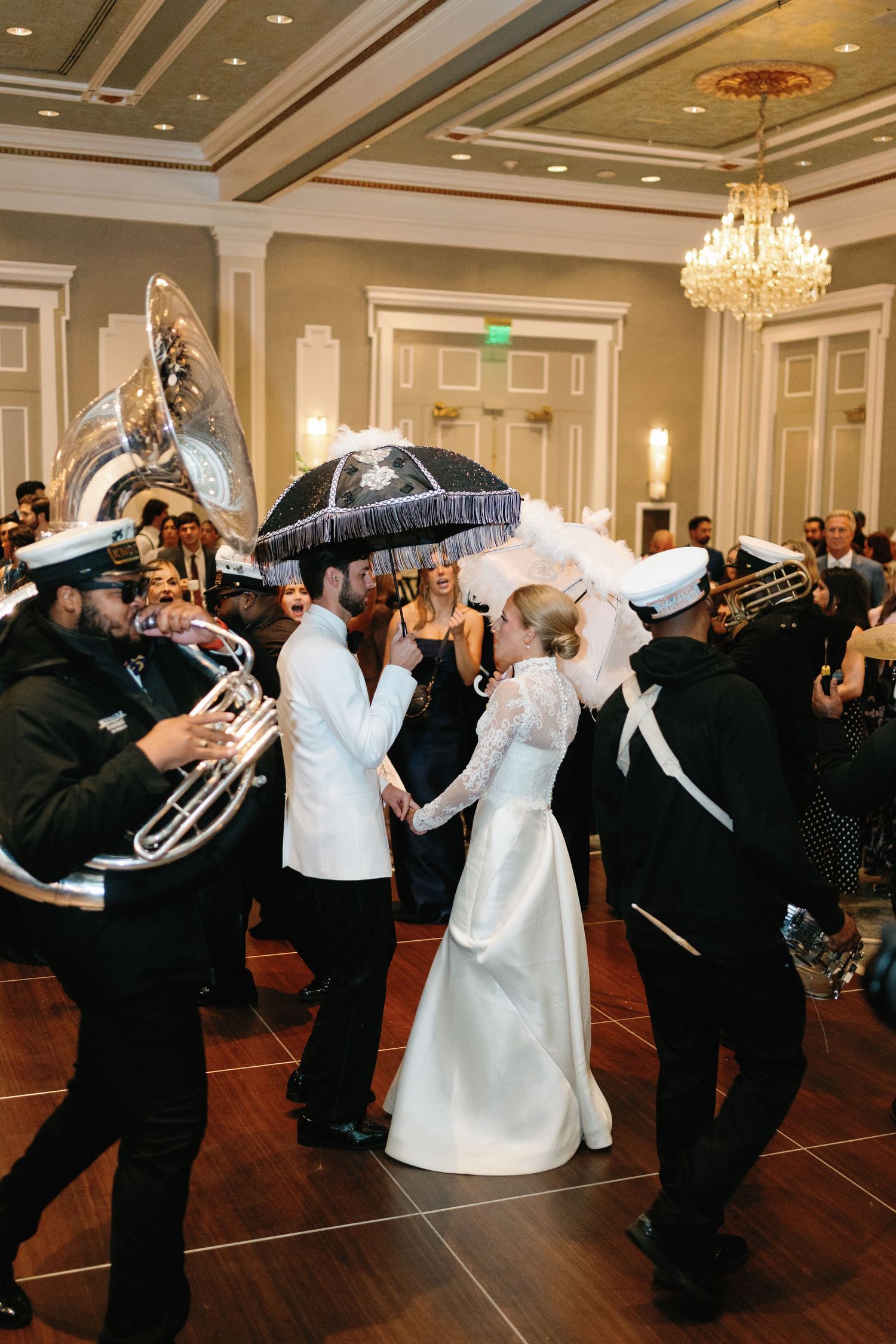 Wedding reception guests performing a festive dance line under crystal chandeliers in a ballroom.