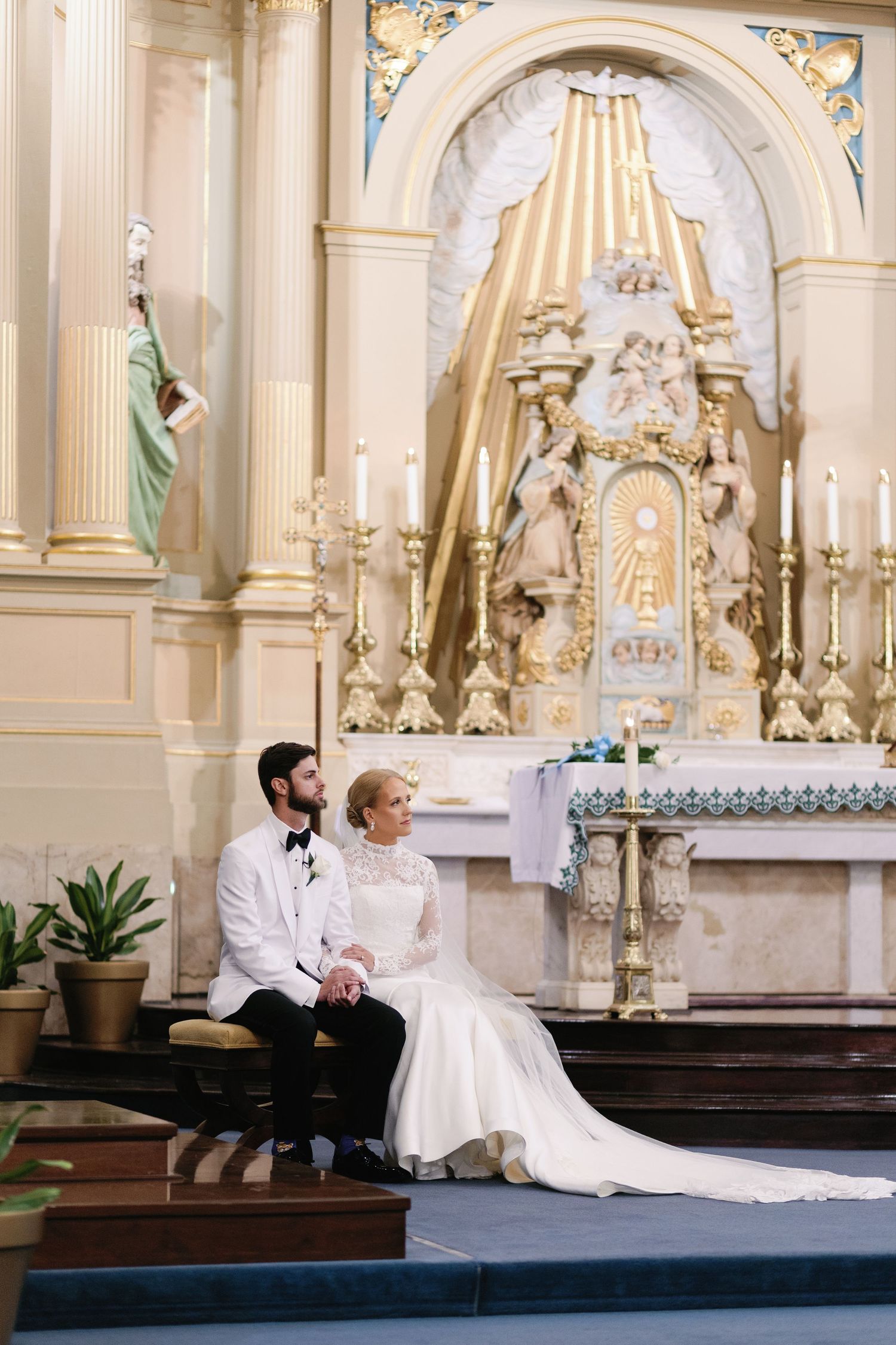 Wedding couple resting on church altar steps in ornate cathedral setting.