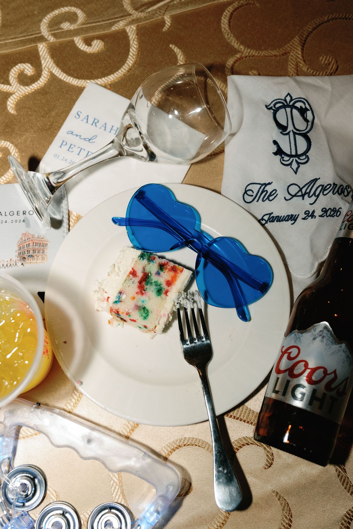 Wedding reception table setting with blue sunglasses, cake slice, Coors Light beer and personalized napkin details.