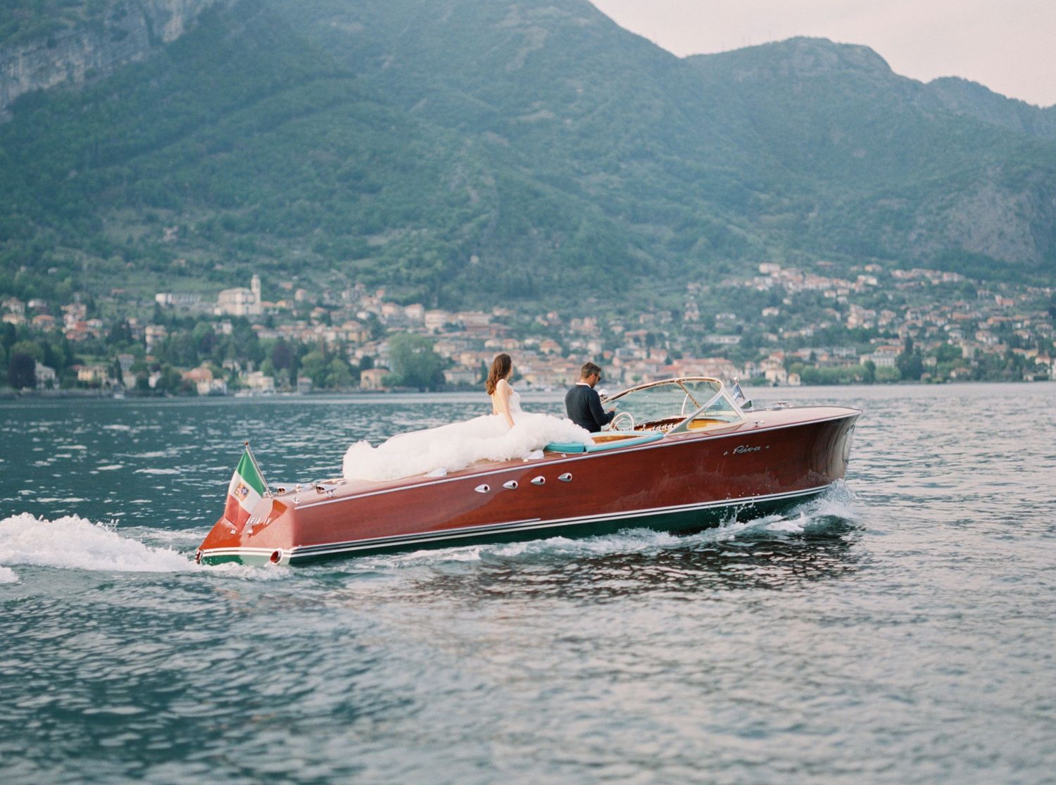 Vintage Riva boat gliding across blue waters near Italian mountain coastline.