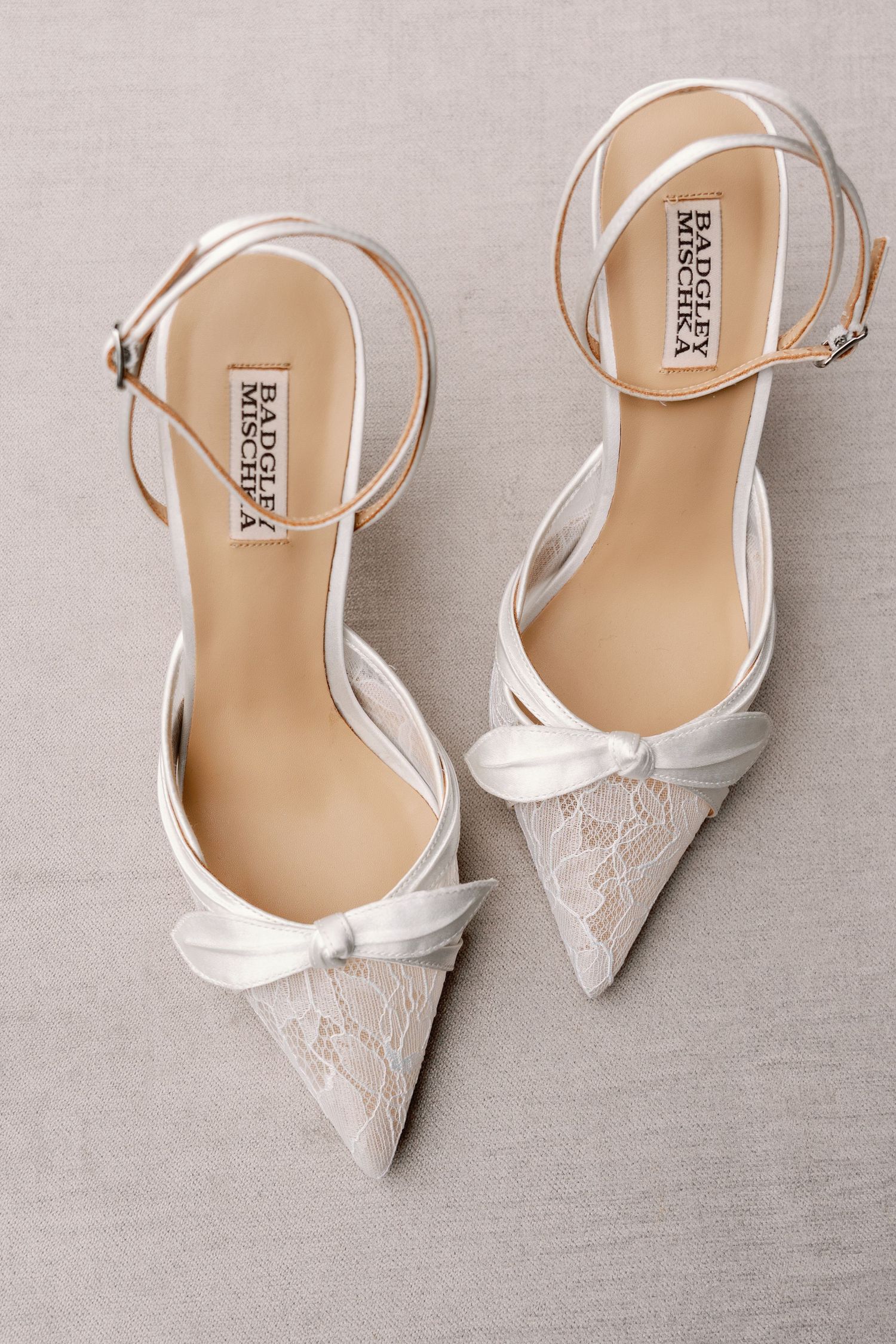 White lace bridal shoes with ankle straps displayed on neutral gray background.