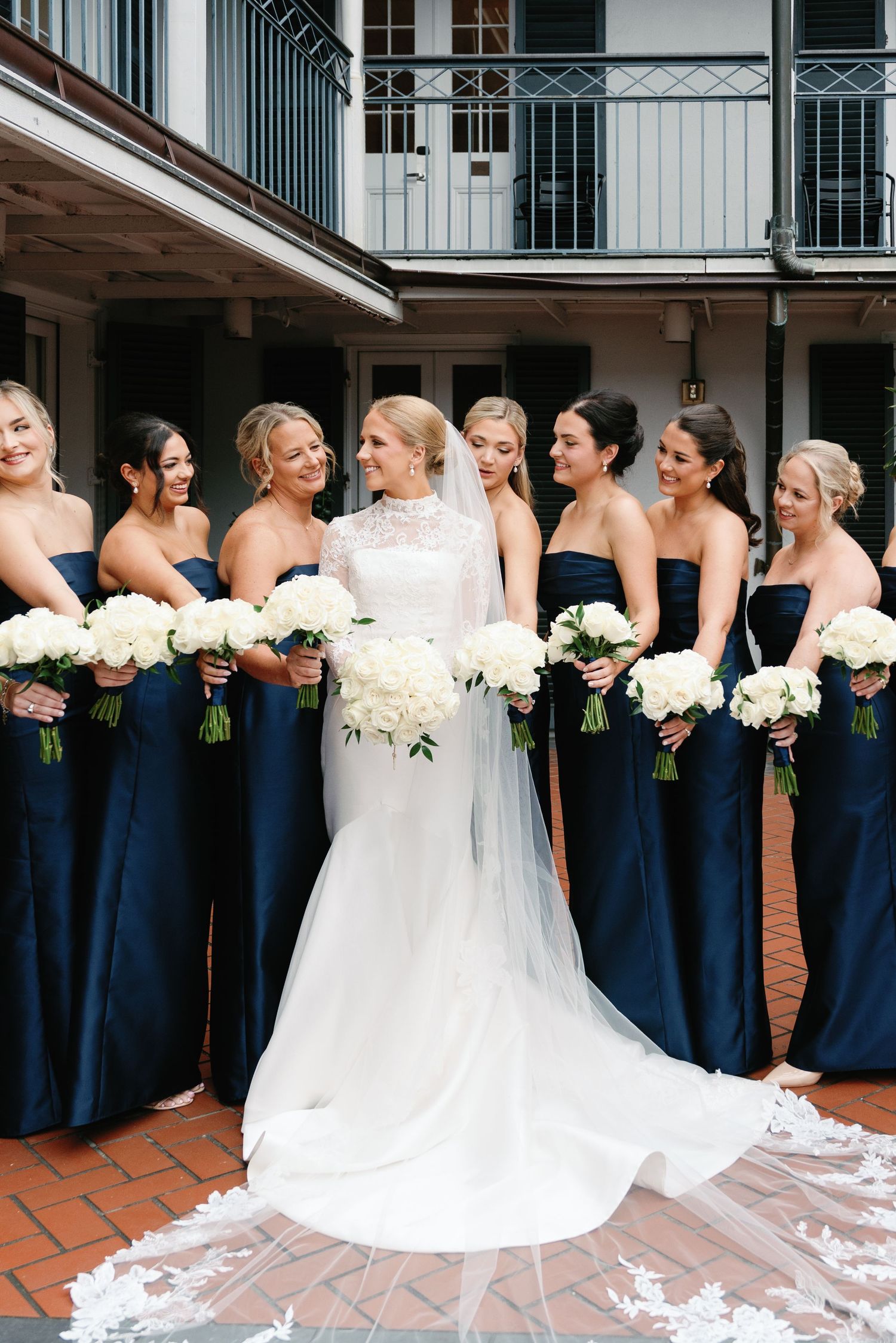 Bridesmaids in navy dresses holding white bouquets pose with bride in flowing gown.