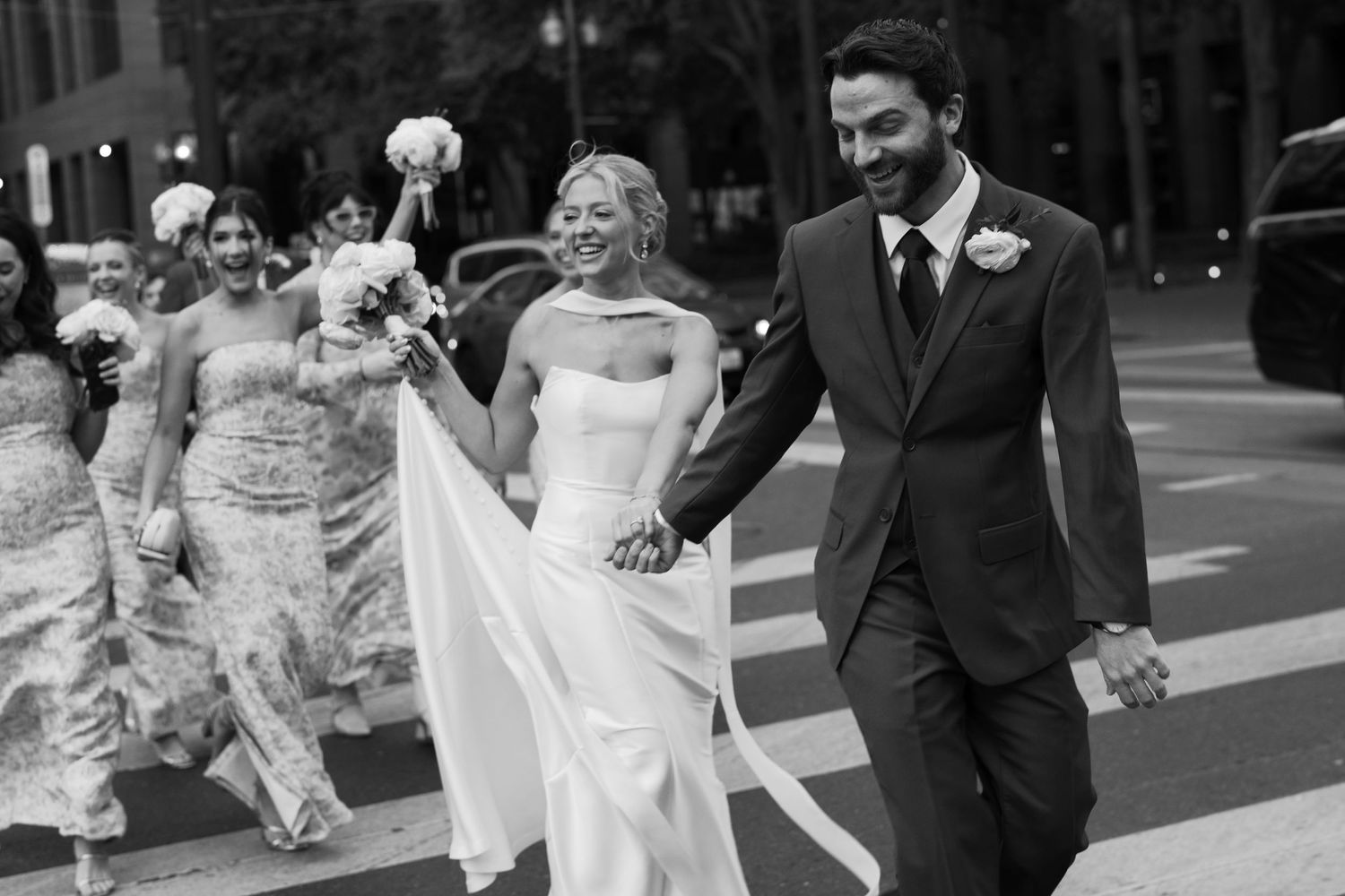 Black and white photo of wedding party celebrating on urban sidewalk.