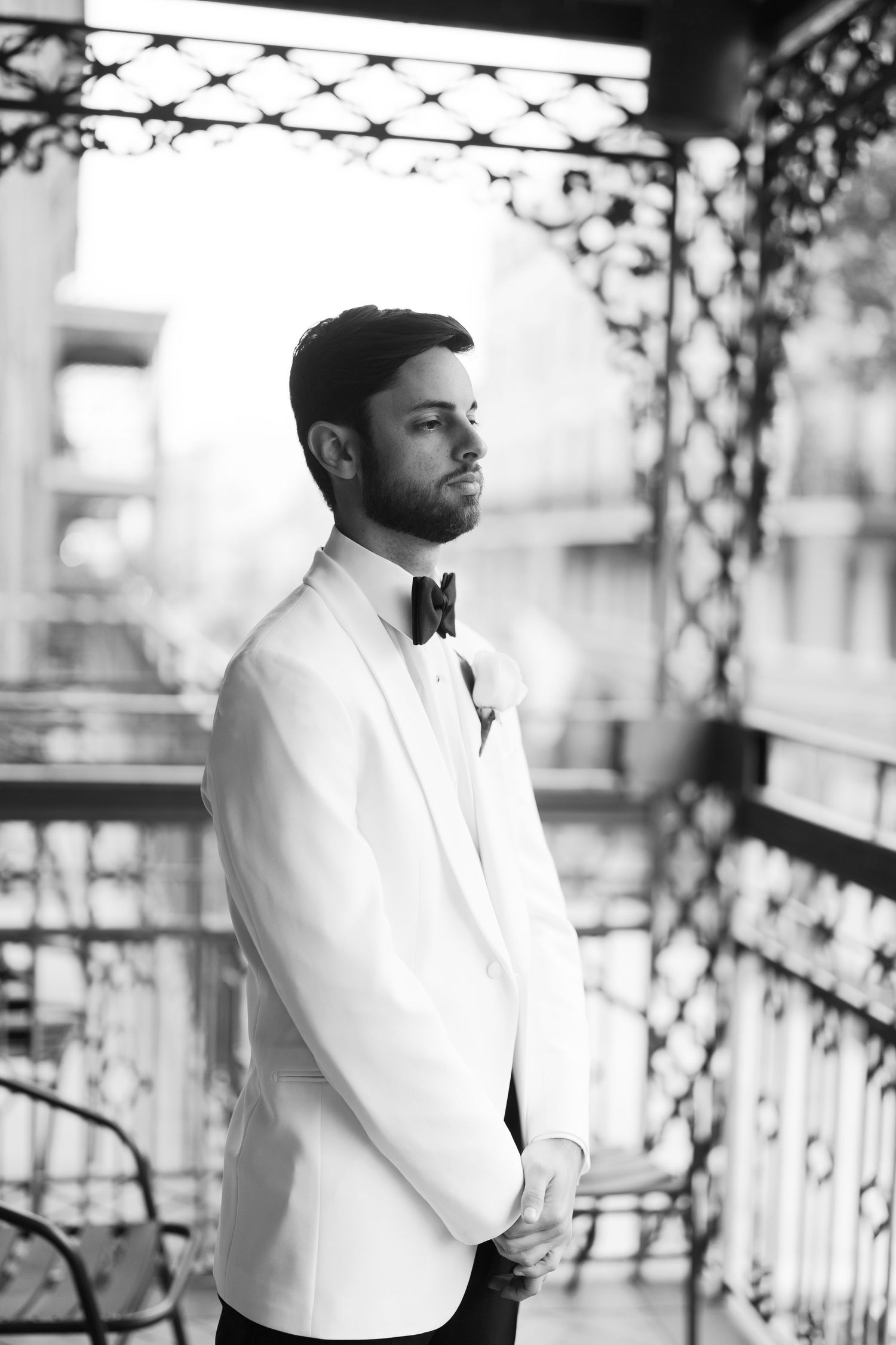 Black and white portraits of groom in white jacket on outdoor balcony.