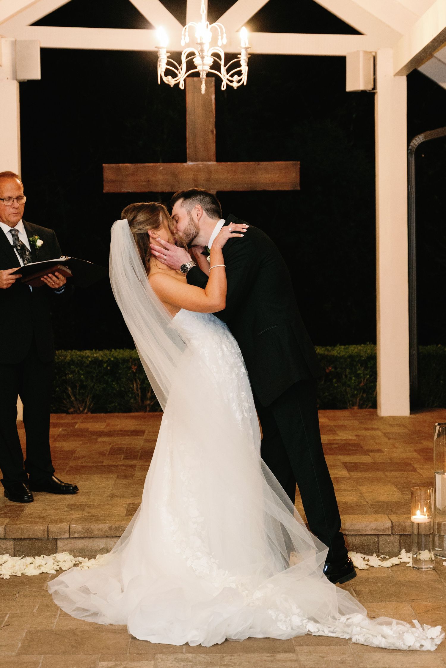 Dramatic dip kiss during wedding ceremony under white pergola with candlelit aisle.