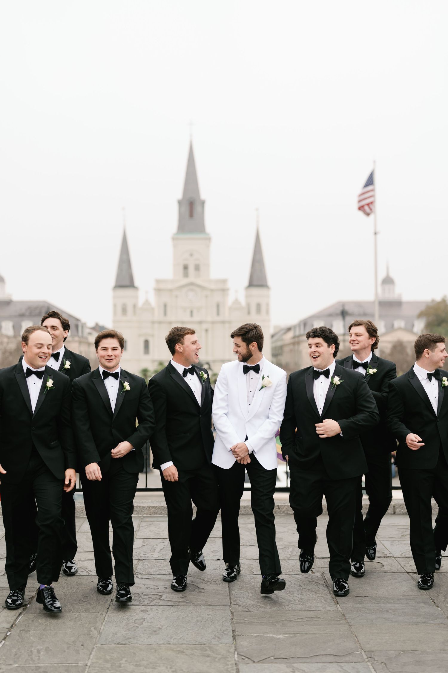 Groomsmen in black tuxedos jumping in sync with St. Louis Cathedral in background.