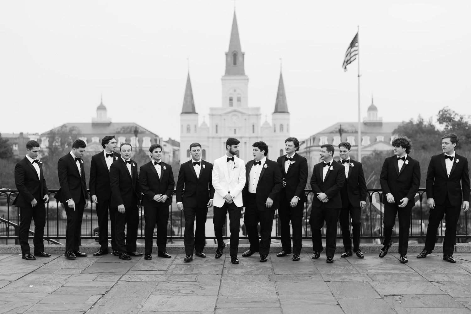 Wedding party in black and white tuxedos lined up against historic New Orleans backdrop with St. Louis Cathedral.