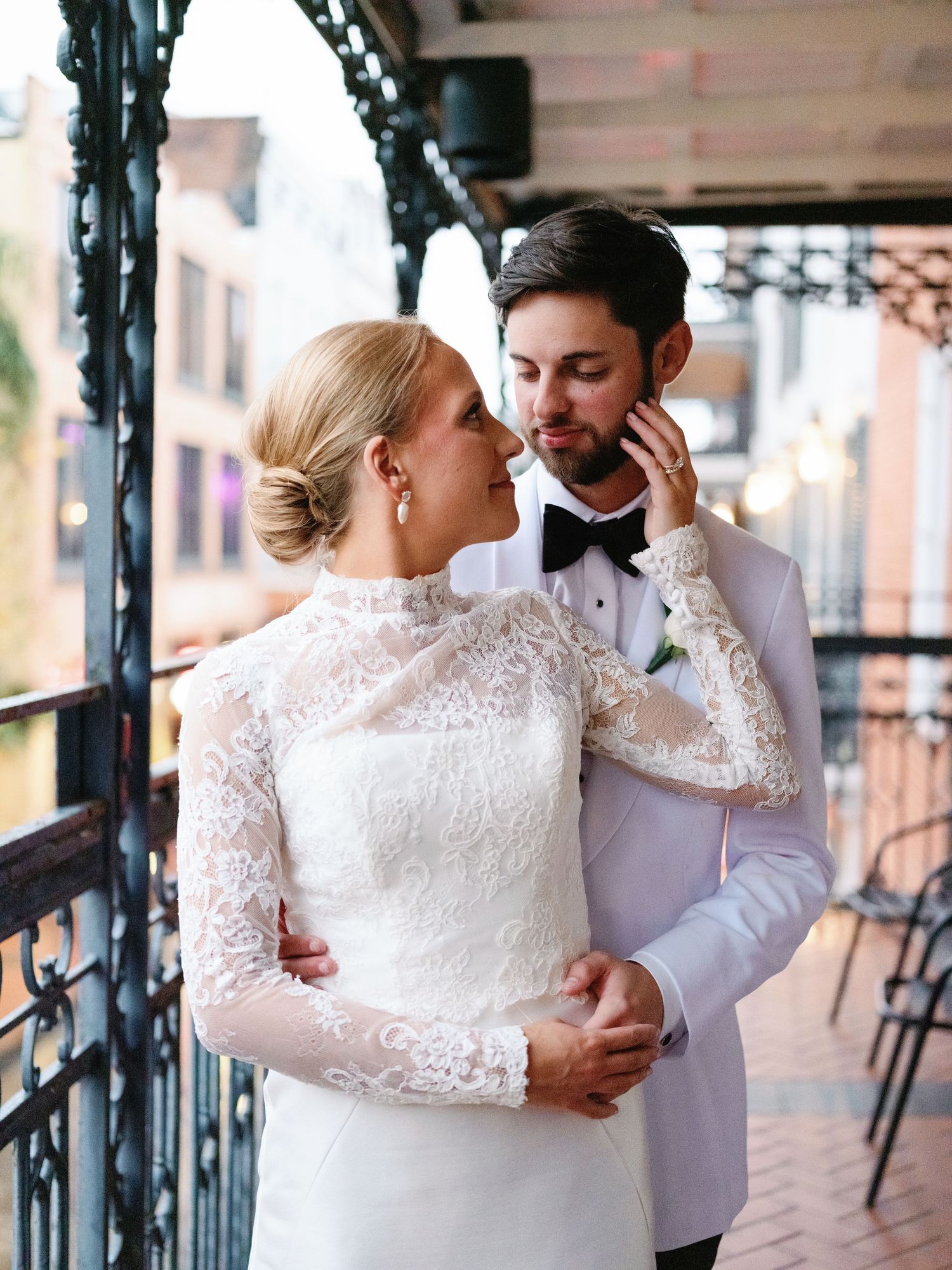A couple shares intimate moments in formal wedding attire on an elegant covered balcony.