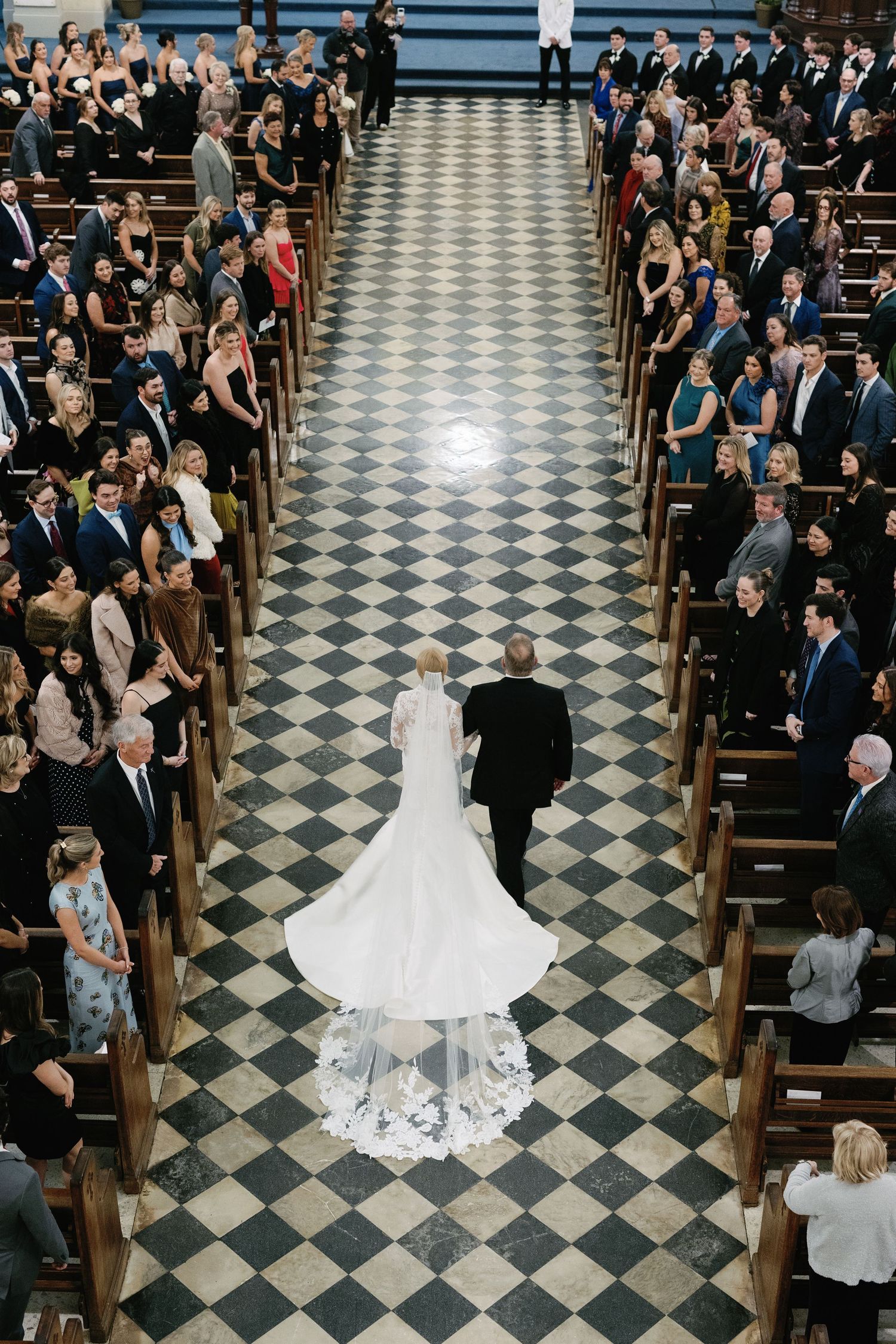 Aerial view of wedding ceremony in church with black and white checkered floor and filled pews.