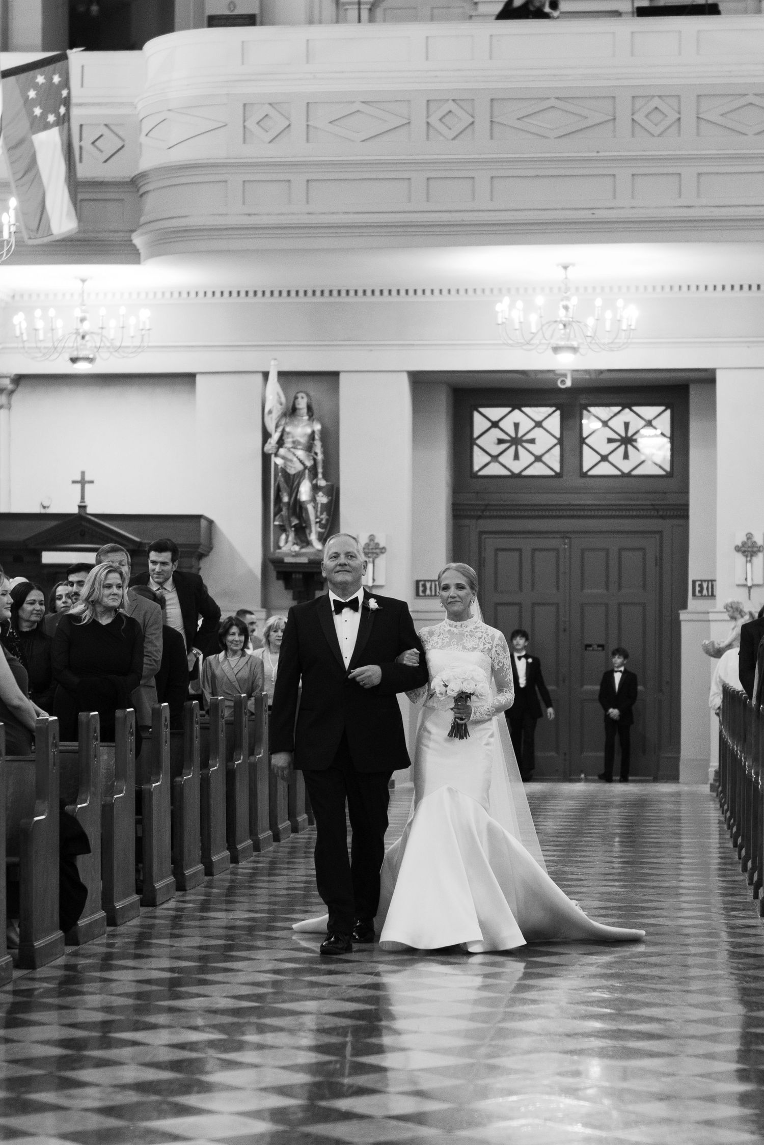 Black and white photo of wedding processional down church aisle with ornate architectural details.
