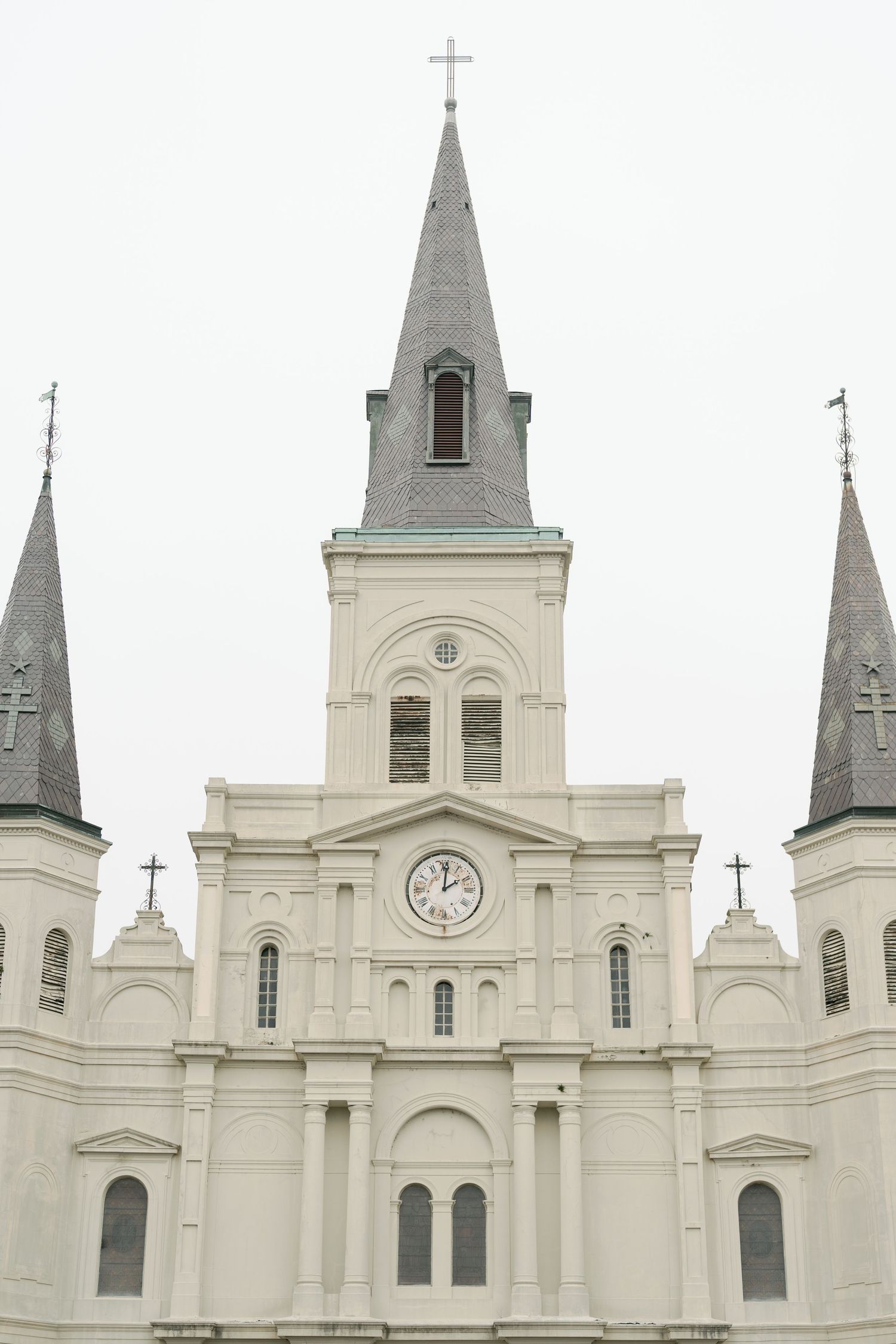 St. Louis Cathedral's white spires and clock tower against overcast sky.