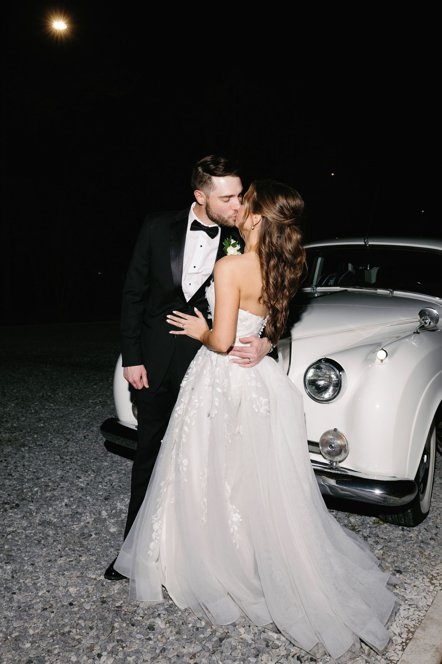 Romantic nighttime wedding photos beside a classic white vintage car.
