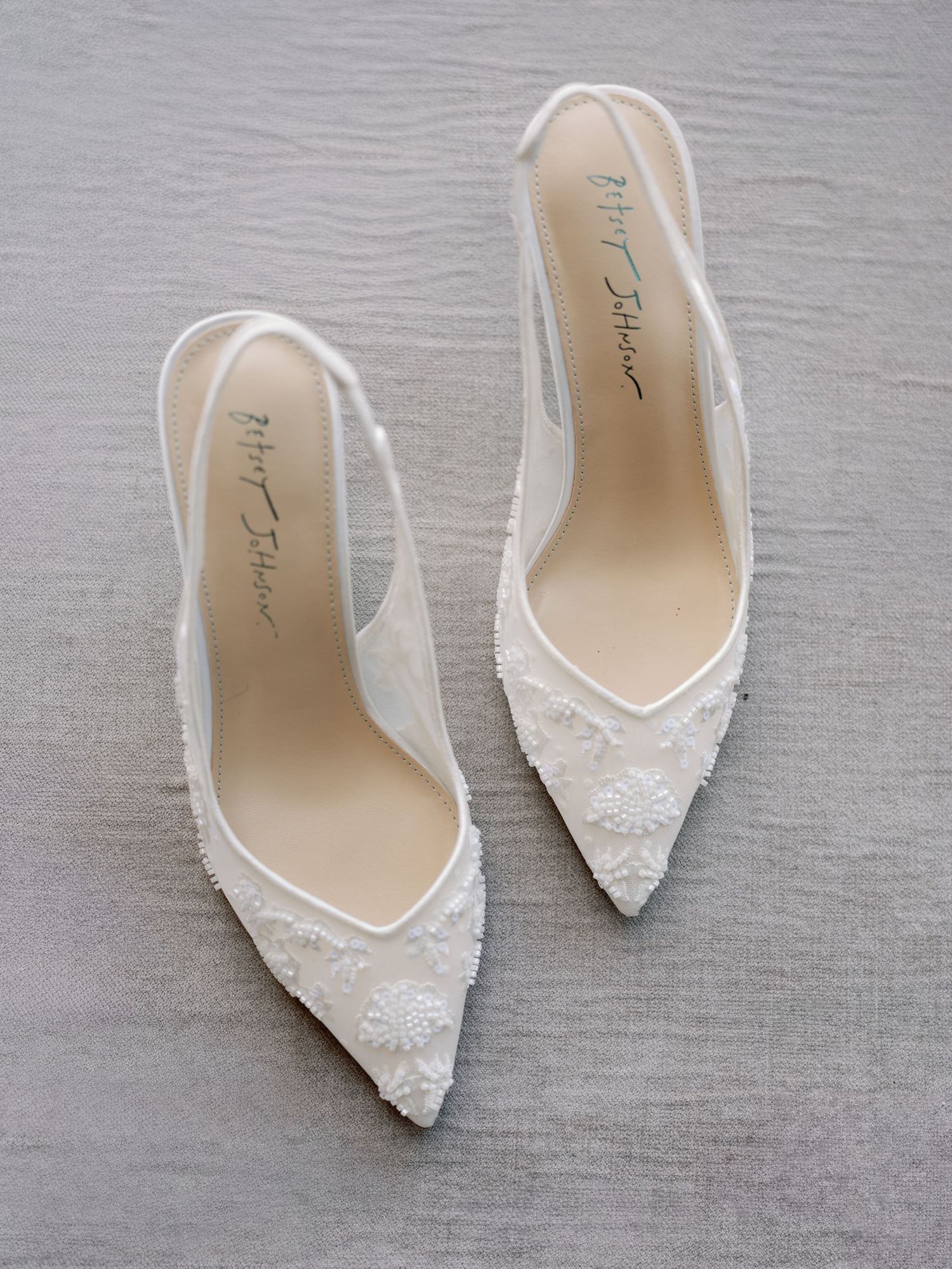 Elegant white lace bridal shoes displayed on a gray background.