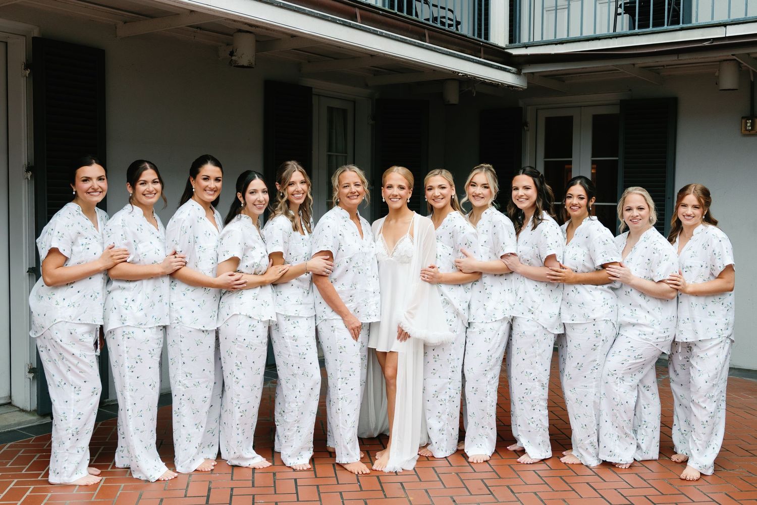 A group of healthcare workers in white uniforms stand together smiling on a brick patio outside a medical facility.