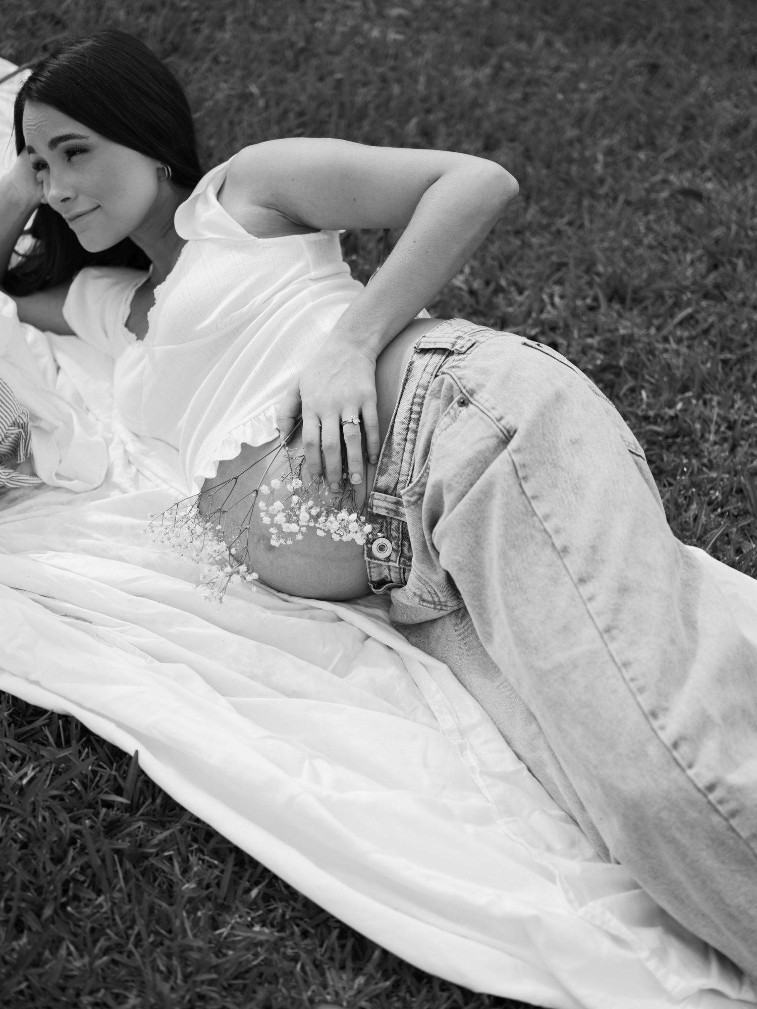 A series of black and white photographs showing someone in a white dress lying on grass in different artistic poses.