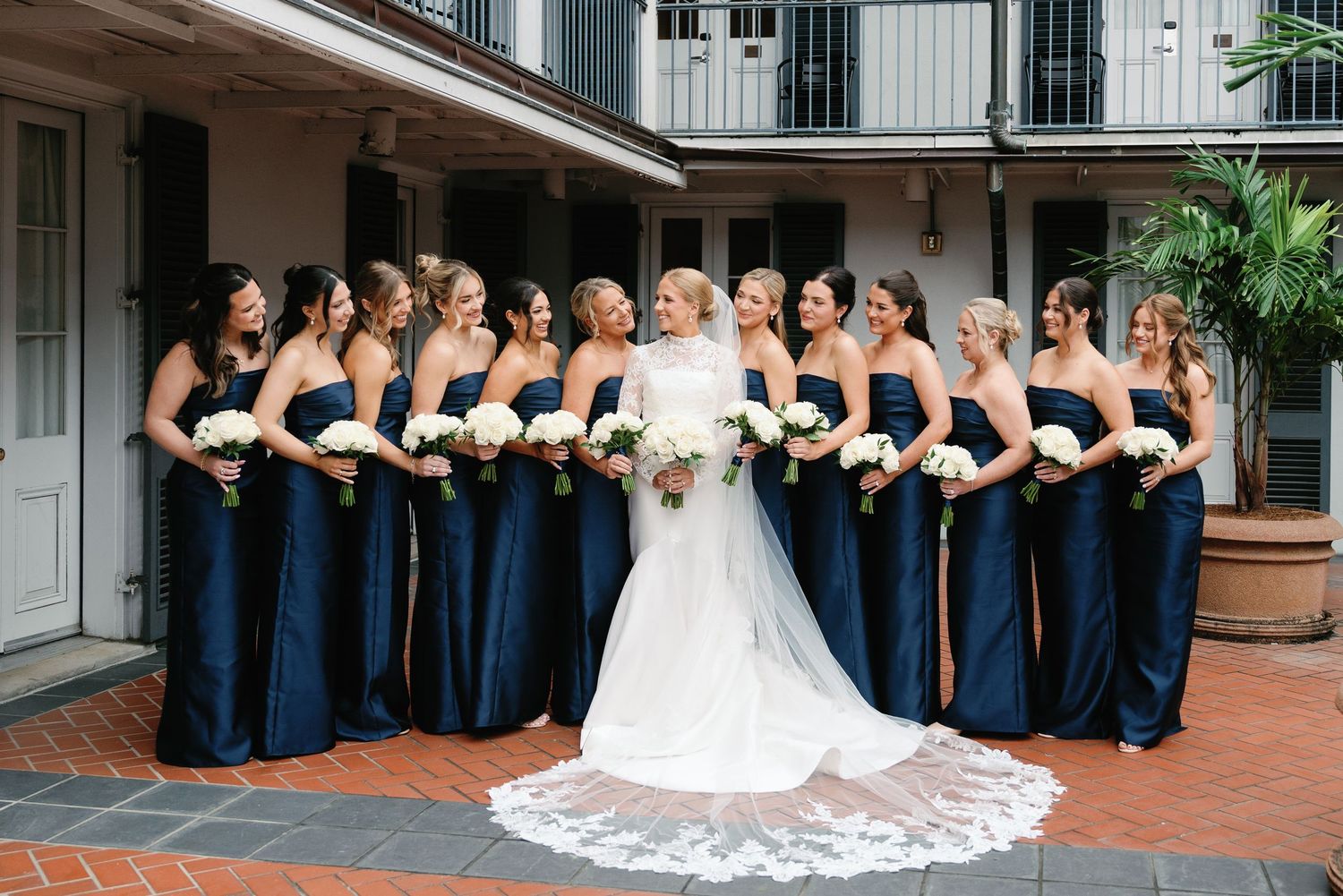 Wedding party in navy blue dresses and white gown pose together in a courtyard setting.