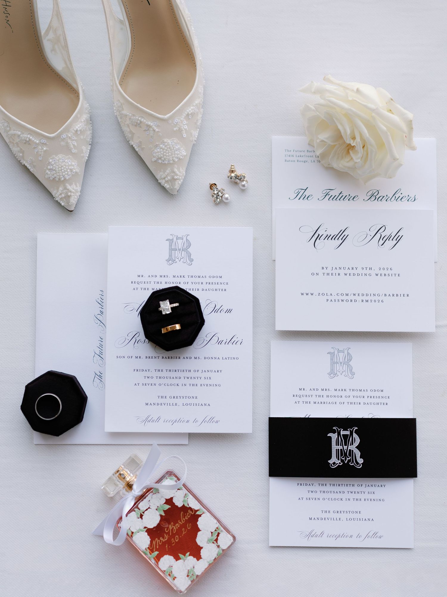 Wedding stationery and accessories arranged with white lace shoes and black velvet ring boxes.