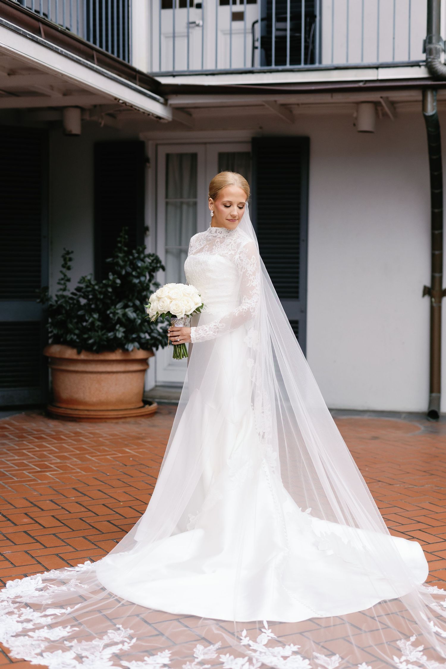 Wedding dress with dramatic cathedral train displayed on brick courtyard.