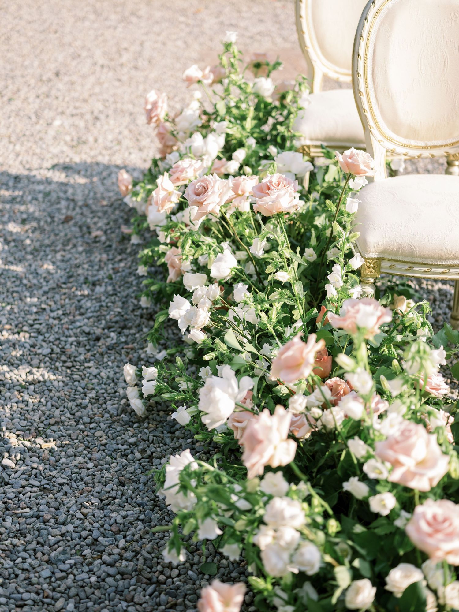 Romantic floral arrangement with pink roses and white flowers on gravel ground.