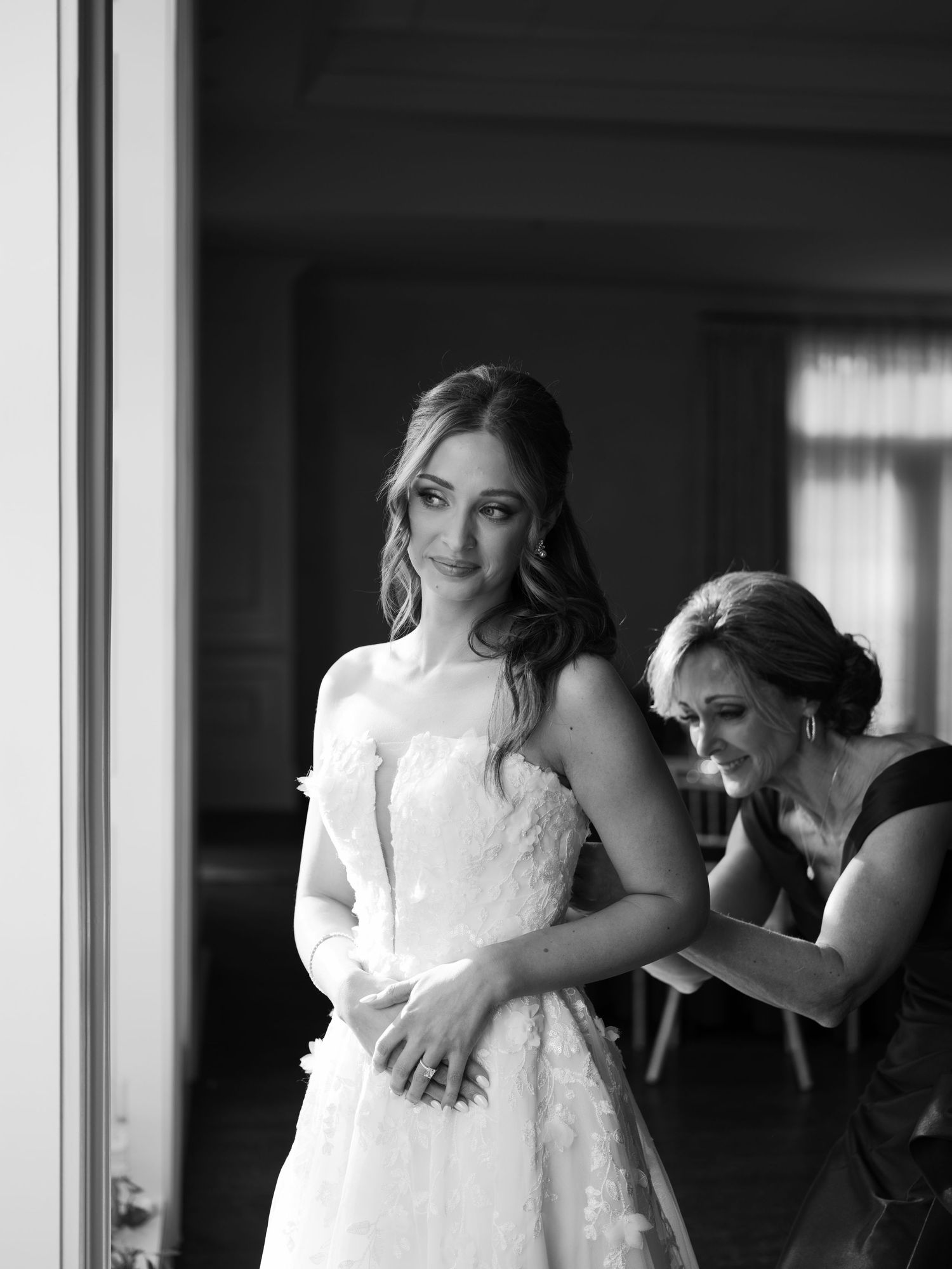 Black and white photo of wedding dress preparation in sunlit room.
